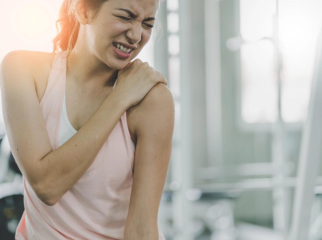 young woman at gym grabbing her shoulder in pain - Baytown, TX Orthopaedic Hand, Wrist & Elbow Surgery