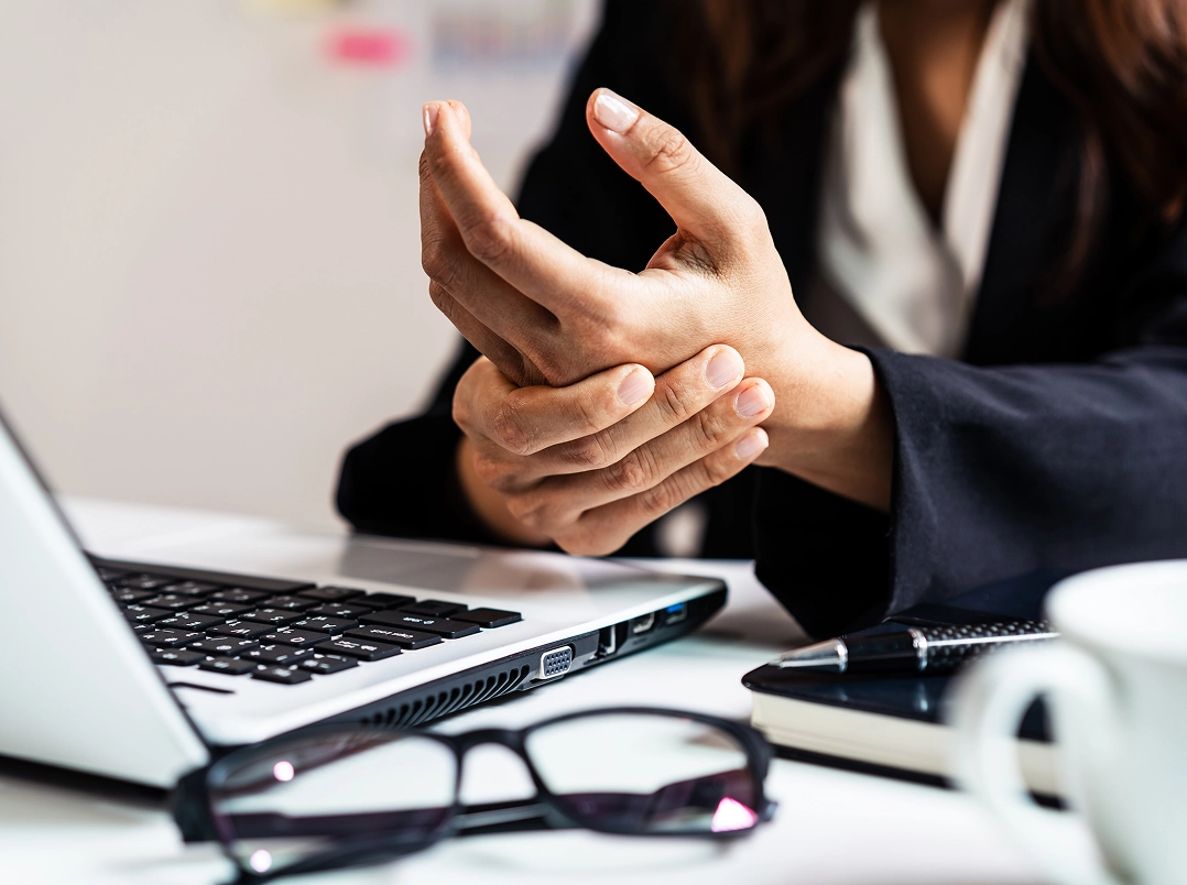 Woman in front of laptop holding hand in pain